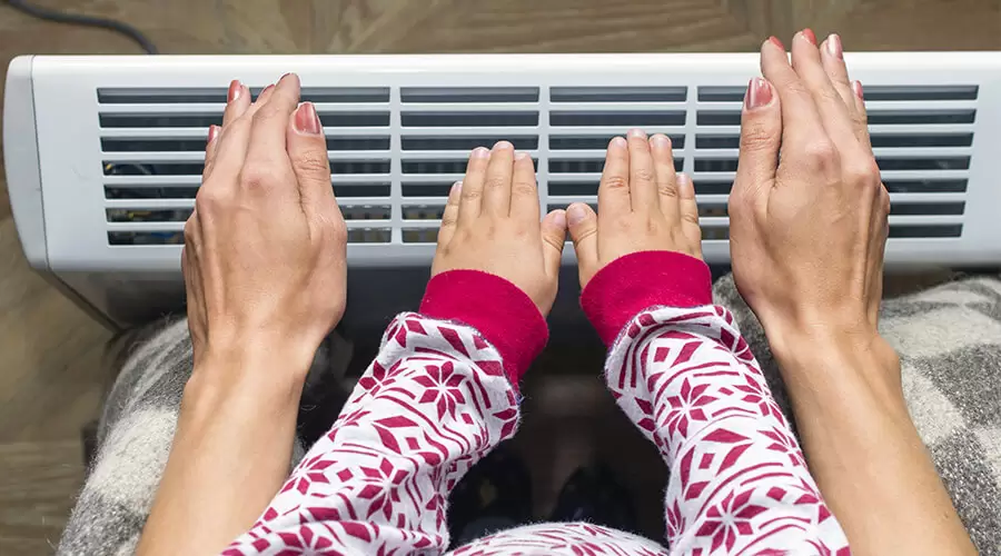 child and mother heating hands on electrical heater